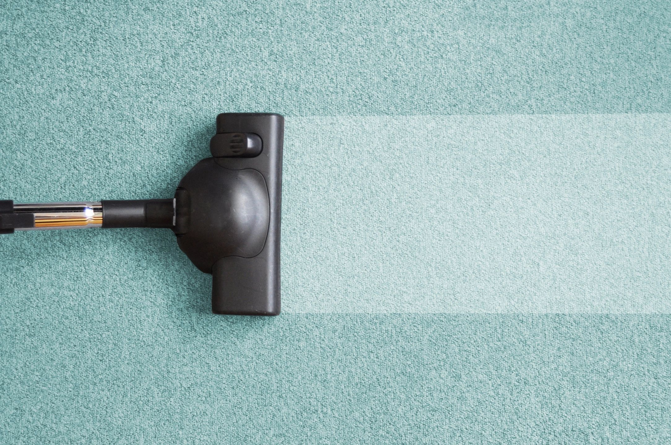 A vacuum cleaner head in use on a light blue carpet, creating a clean, bright path compared to the uncleaned area.